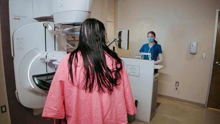 dark-haired women in pink scrubs standing by a mammogram machine as a dark-haired women in blue scrubs mans the machine.